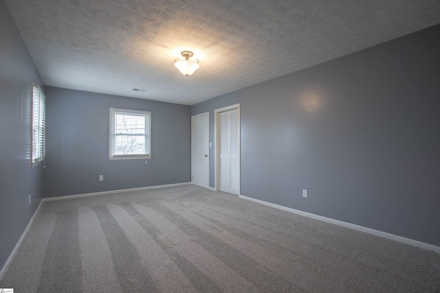 spare room with carpet, visible vents, baseboards, and a textured ceiling