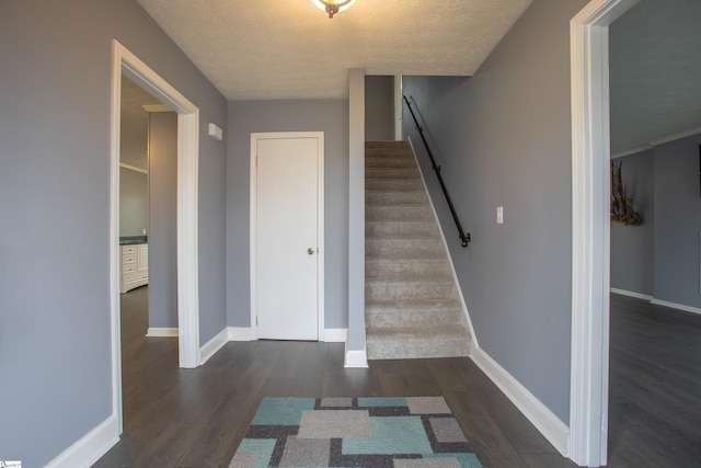 stairway with a textured ceiling, wood finished floors, and baseboards