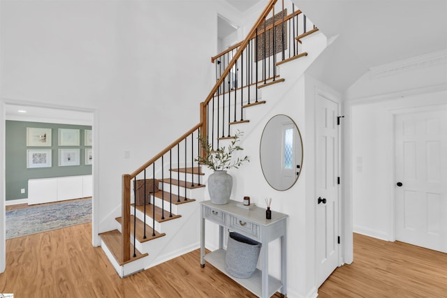 stairway featuring a towering ceiling, baseboards, and wood finished floors
