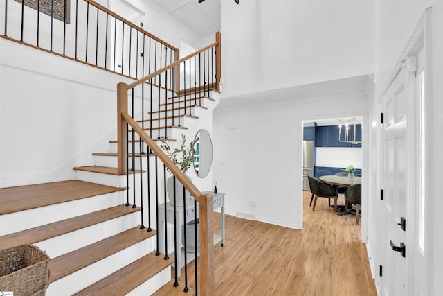 staircase with a towering ceiling, baseboards, crown molding, and wood finished floors