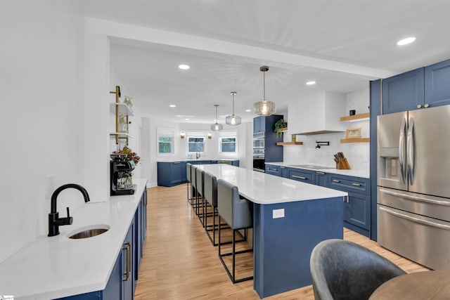 kitchen featuring open shelves, a sink, a breakfast bar, appliances with stainless steel finishes, and blue cabinetry
