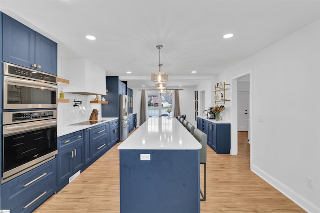 kitchen with light wood-style flooring, appliances with stainless steel finishes, blue cabinetry, and a kitchen breakfast bar