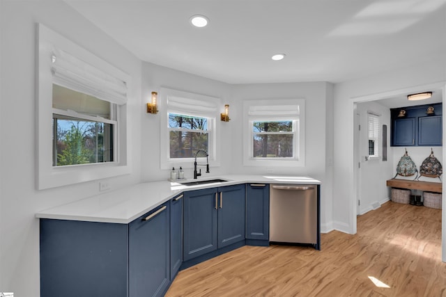 kitchen with stainless steel dishwasher, light wood-style flooring, blue cabinets, a sink, and light countertops
