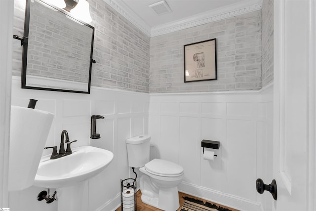 bathroom featuring a decorative wall, visible vents, toilet, a sink, and wainscoting