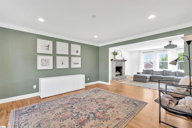 living area with baseboards, recessed lighting, crown molding, a fireplace with raised hearth, and wood finished floors