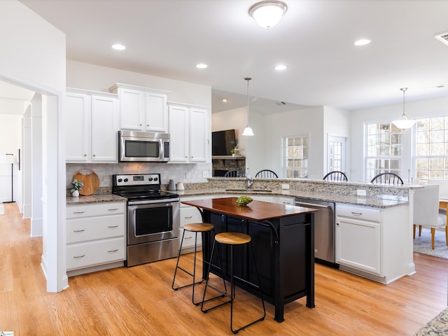 kitchen featuring a breakfast bar, a peninsula, light wood-style floors, appliances with stainless steel finishes, and a sink