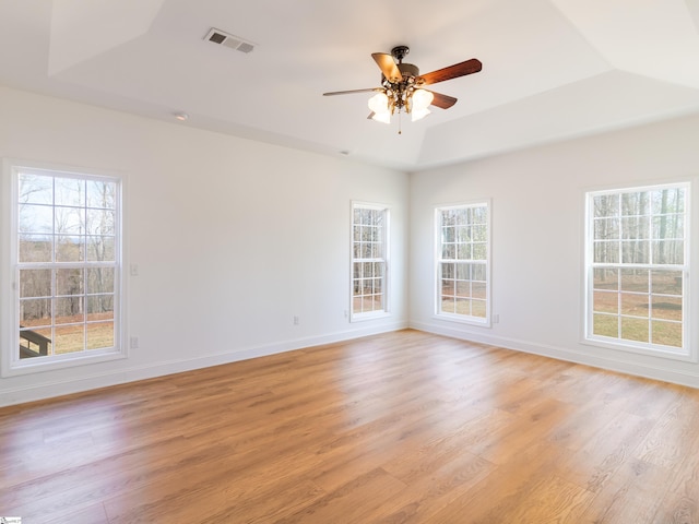 empty room featuring light wood-style flooring, a ceiling fan, visible vents, a raised ceiling, and baseboards