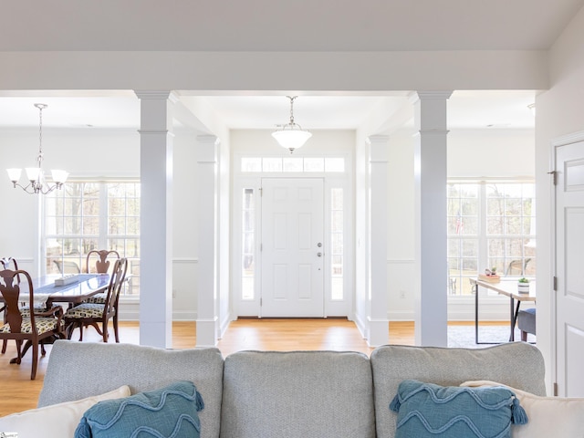 foyer entrance featuring ornate columns, an inviting chandelier, and light wood-style floors