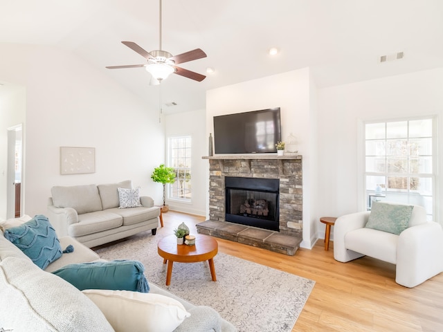 living area featuring a stone fireplace, vaulted ceiling, a ceiling fan, visible vents, and wood finished floors