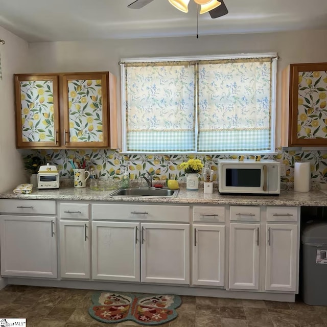 kitchen with white microwave, ceiling fan, white cabinets, a sink, and decorative backsplash