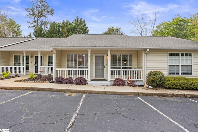 ranch-style house featuring a porch, uncovered parking, and a shingled roof