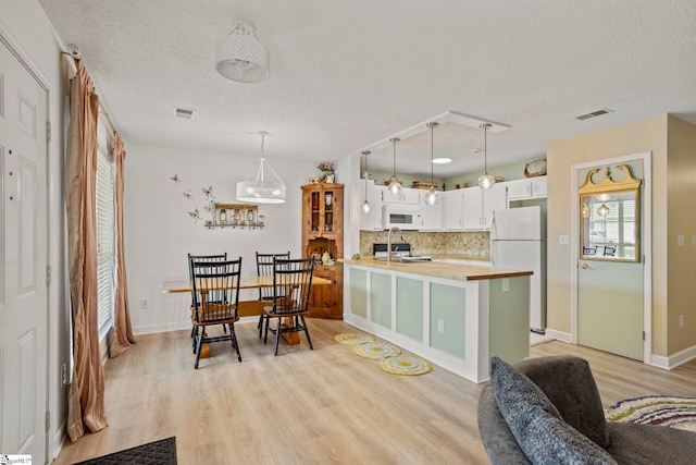 kitchen featuring white appliances, a peninsula, light wood-style flooring, visible vents, and a sink