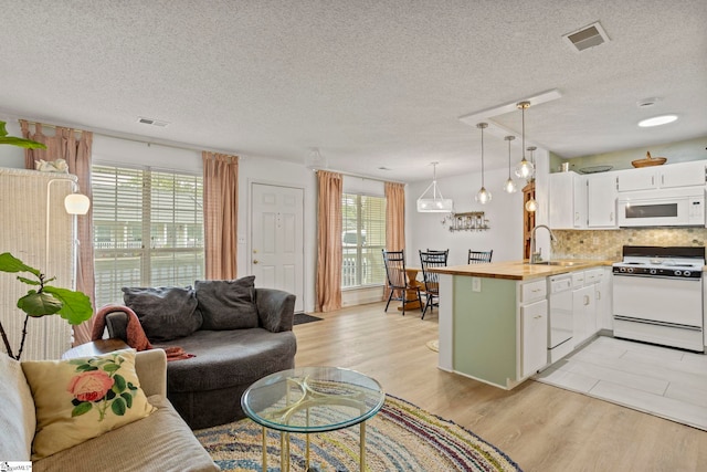 living area featuring light wood-type flooring, visible vents, and a textured ceiling