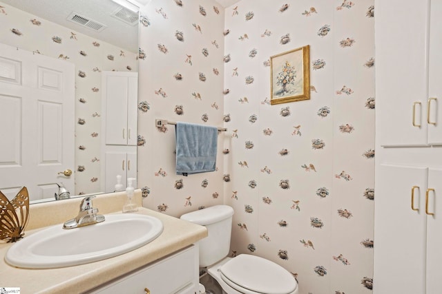 bathroom featuring visible vents, toilet, vanity, and wallpapered walls