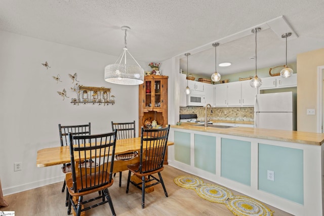 dining room featuring baseboards, light wood-type flooring, and a textured ceiling