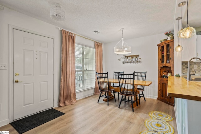 dining area with visible vents, light wood-style flooring, baseboards, and a textured ceiling