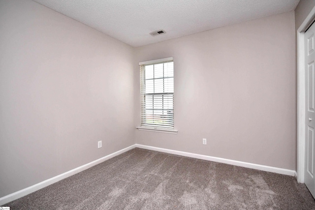 empty room featuring a textured ceiling, visible vents, dark colored carpet, and baseboards