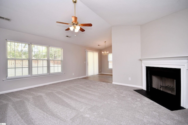 unfurnished living room featuring visible vents, ceiling fan with notable chandelier, a fireplace with flush hearth, vaulted ceiling, and carpet flooring