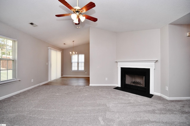 unfurnished living room with visible vents, carpet floors, vaulted ceiling, ceiling fan with notable chandelier, and a fireplace with flush hearth
