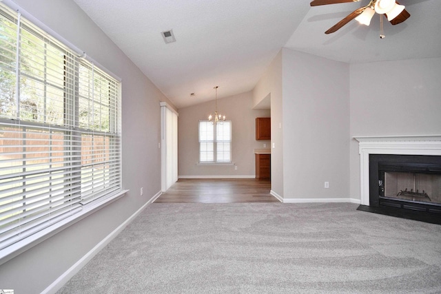 unfurnished living room featuring ceiling fan with notable chandelier, a fireplace with flush hearth, vaulted ceiling, visible vents, and carpet floors