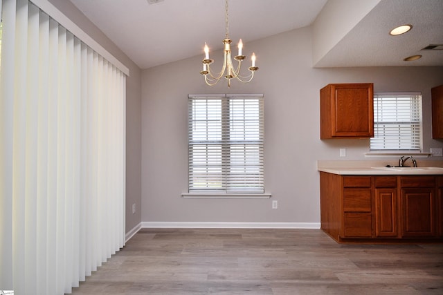 unfurnished dining area featuring light wood-style flooring, a sink, lofted ceiling, and a notable chandelier