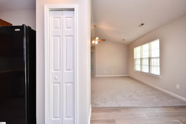 interior space with light wood-type flooring, a ceiling fan, visible vents, vaulted ceiling, and baseboards