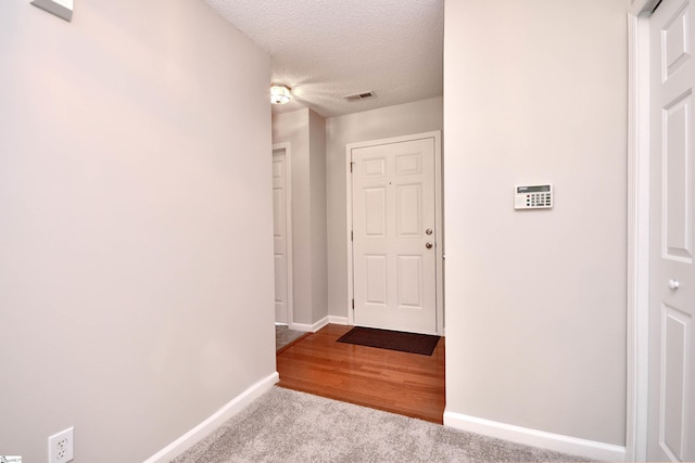 hallway with visible vents, baseboards, carpet, and a textured ceiling