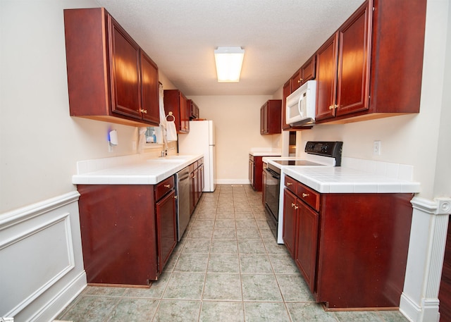 kitchen featuring light countertops, light tile patterned floors, dark brown cabinets, and white appliances