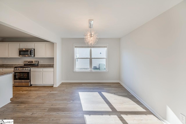 unfurnished dining area with light wood-type flooring, a notable chandelier, and baseboards