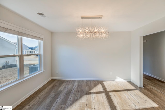 unfurnished dining area featuring baseboards, wood finished floors, a notable chandelier, and visible vents