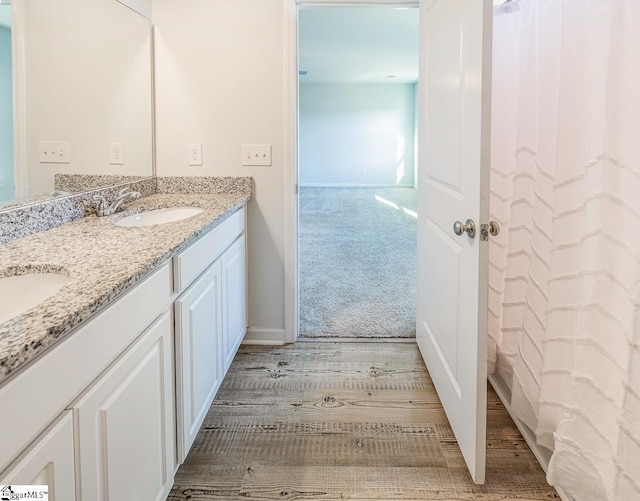 full bath with double vanity, a sink, and wood finished floors
