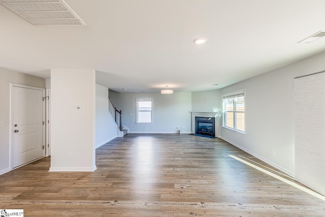 unfurnished living room featuring visible vents, baseboards, wood finished floors, and stairs