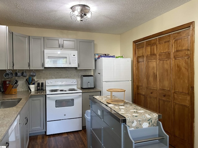 kitchen featuring white appliances, dark wood-type flooring, gray cabinets, a textured ceiling, and a sink