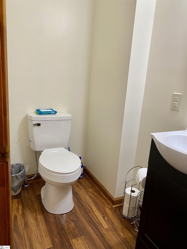 half bathroom featuring baseboards, wood finished floors, toilet, and vanity