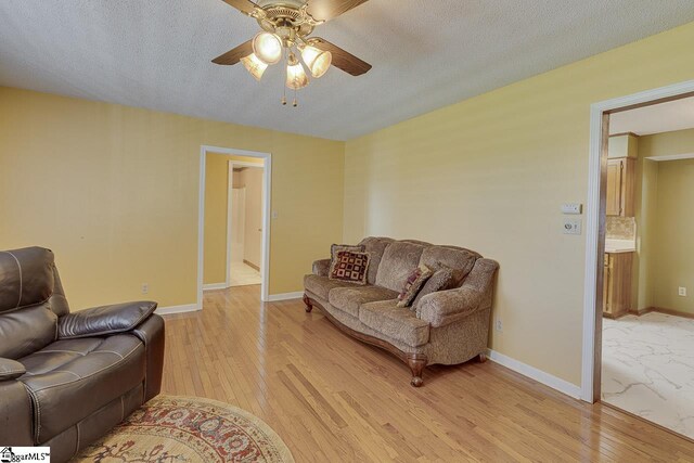 living room featuring light wood-style flooring, ceiling fan, and baseboards