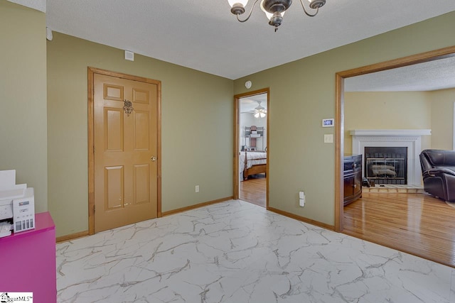 interior space featuring an inviting chandelier, a fireplace, a textured ceiling, marble finish floor, and baseboards