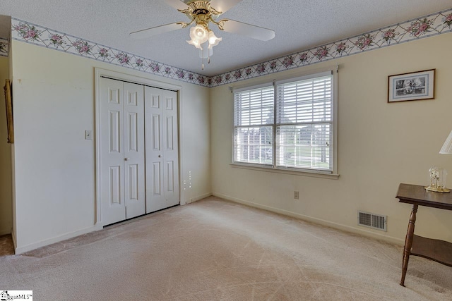 unfurnished bedroom with a textured ceiling, a closet, carpet, and visible vents