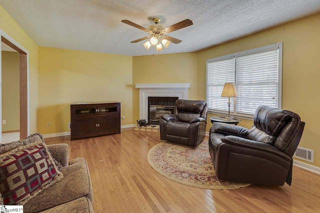 living area with a glass covered fireplace, baseboards, a ceiling fan, light wood-style floors, and visible vents