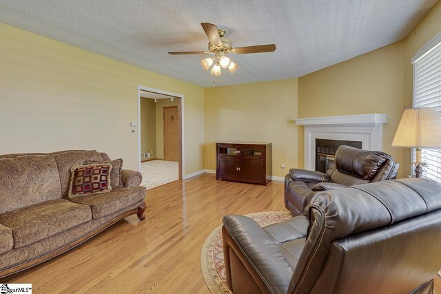 living room featuring light wood-style floors, ceiling fan, a fireplace, and a textured ceiling