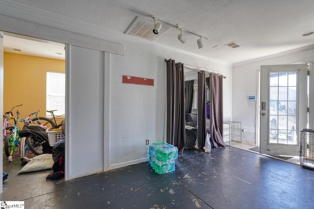 interior space with concrete floors, track lighting, a textured ceiling, crown molding, and visible vents