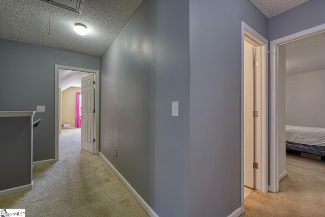corridor with carpet flooring, attic access, a textured ceiling, and baseboards