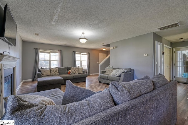 living room featuring wood finished floors, baseboards, a glass covered fireplace, and visible vents