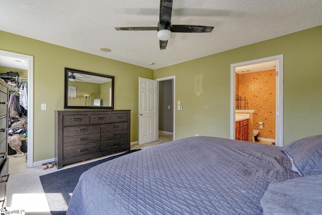 bedroom featuring baseboards, carpet flooring, a textured ceiling, connected bathroom, and a walk in closet