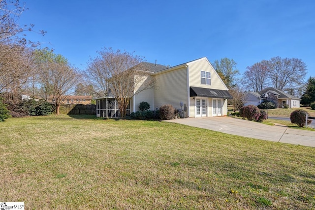view of side of home with fence, a sunroom, and a lawn