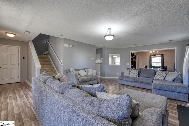 living area with visible vents, wood finished floors, stairs, baseboards, and a notable chandelier