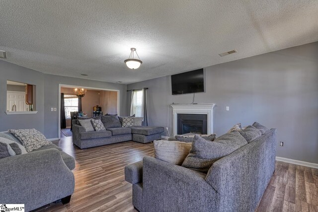 living area with a glass covered fireplace, visible vents, baseboards, and wood finished floors
