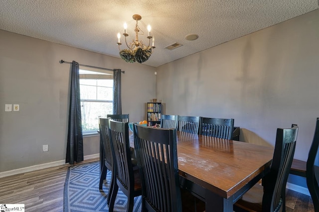 dining area featuring a textured ceiling, visible vents, wood finished floors, baseboards, and a notable chandelier
