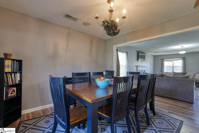 dining space with a textured ceiling, visible vents, a chandelier, wood finished floors, and baseboards