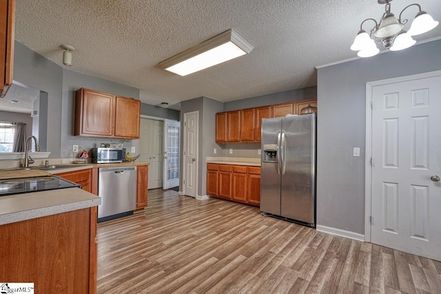 kitchen with a chandelier, light countertops, brown cabinetry, stainless steel appliances, and light wood finished floors