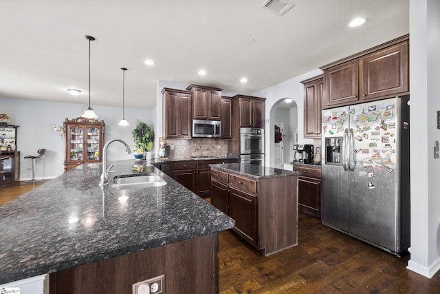 kitchen with arched walkways, a peninsula, a kitchen island, a sink, and stainless steel appliances